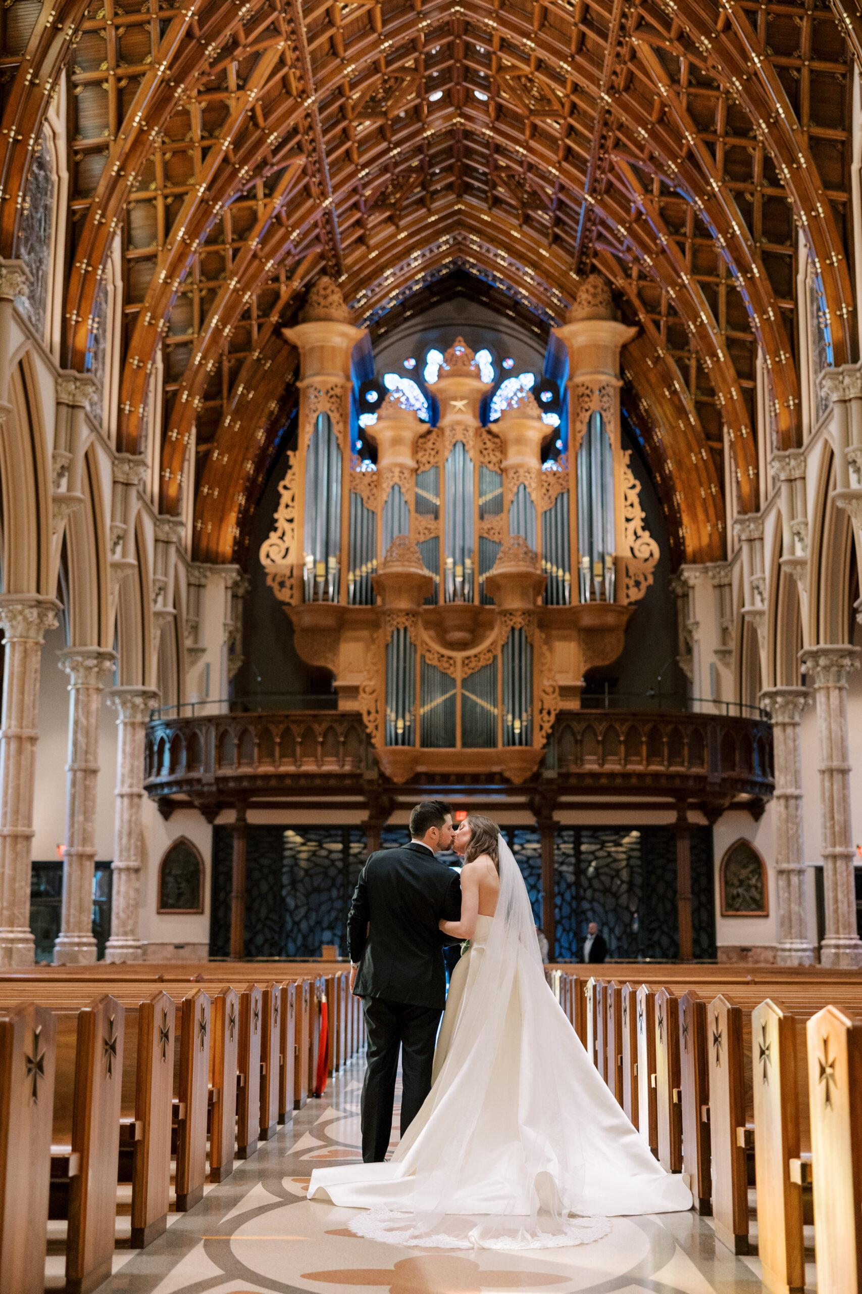 Bride and groom sharing a kiss in the stunning Holy Name Cathedral with a grand organ and vaulted ceilings, during their Blackstone Hotel wedding, planned by Chicago wedding planner Savoir Fête.